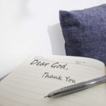 Hands writing “Dear God” in a journal with soft light shining on the page, symbolizing gratitude and worship to the God who sees.
