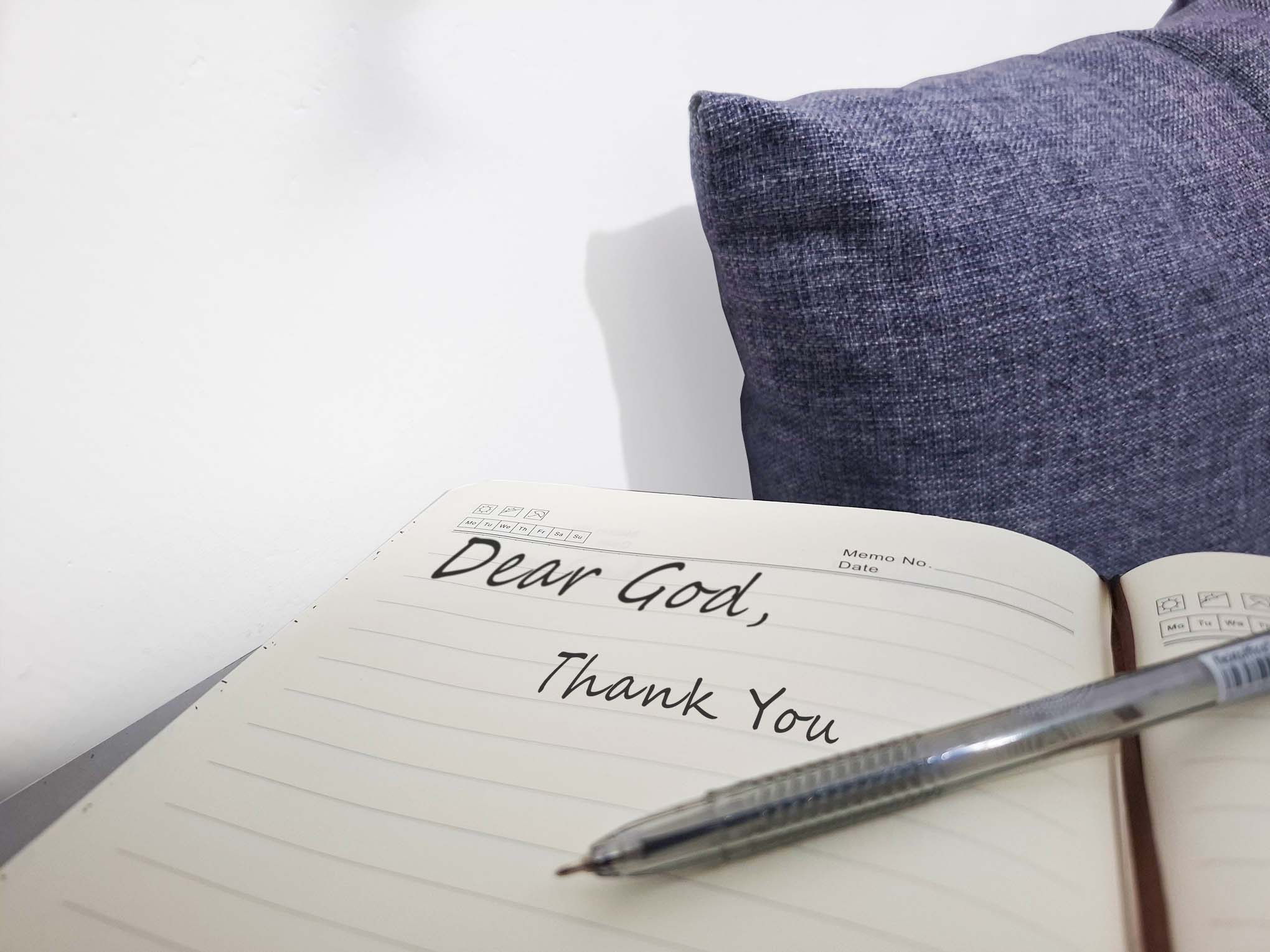 Hands writing “Dear God” in a journal with soft light shining on the page, symbolizing gratitude and worship to the God who sees.